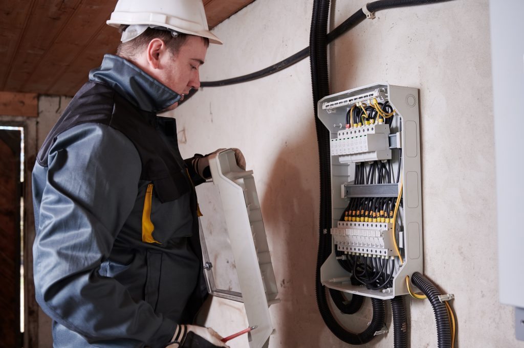 Male electrician checking switchboard in basement.